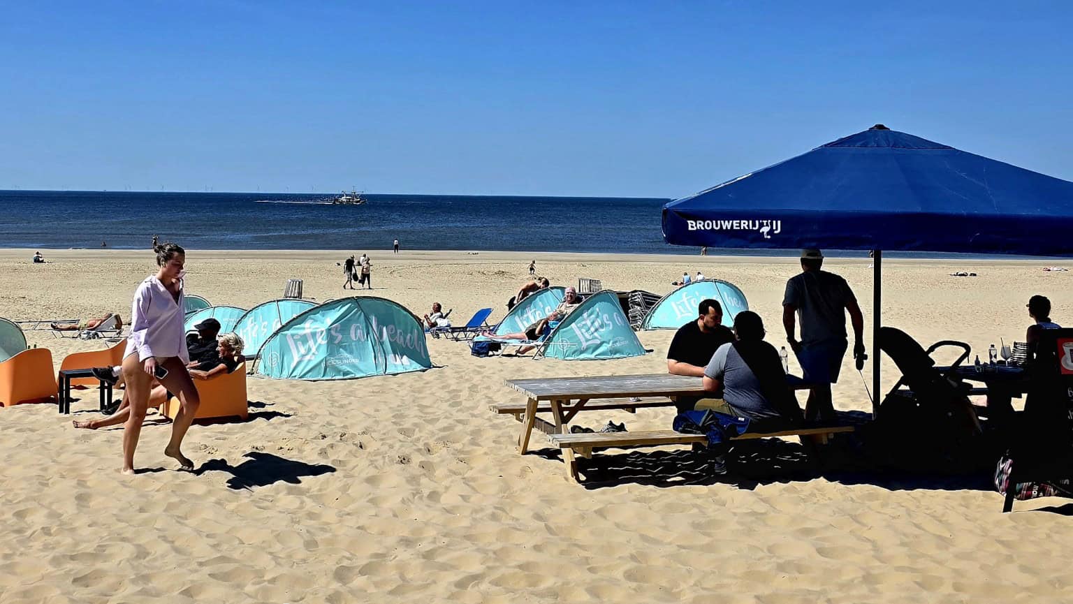 Strandbezoekers genieten onder parasols van zonnig en warm weer in juni